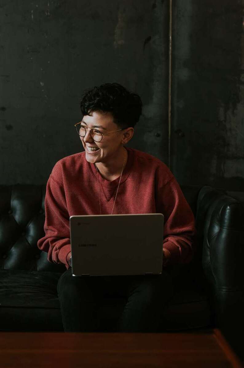 A person sitting on a dark green chair with a laptop on their knee