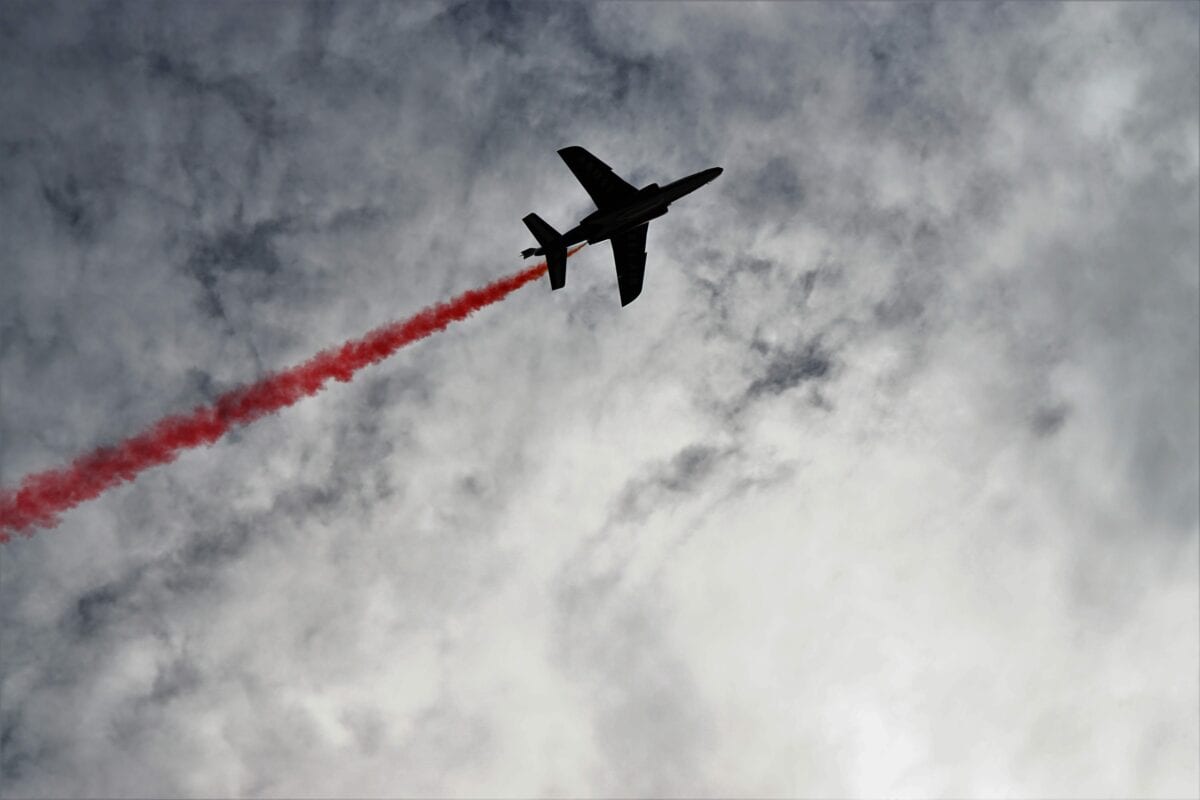 An image of a jet in the sky with a bright red contrail.