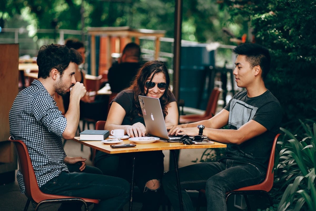 “Three people at a coffee shop table looking over a computer.”