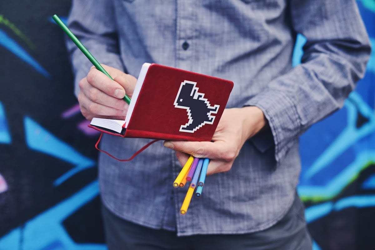 Person writing in a notebook with colored pencils.