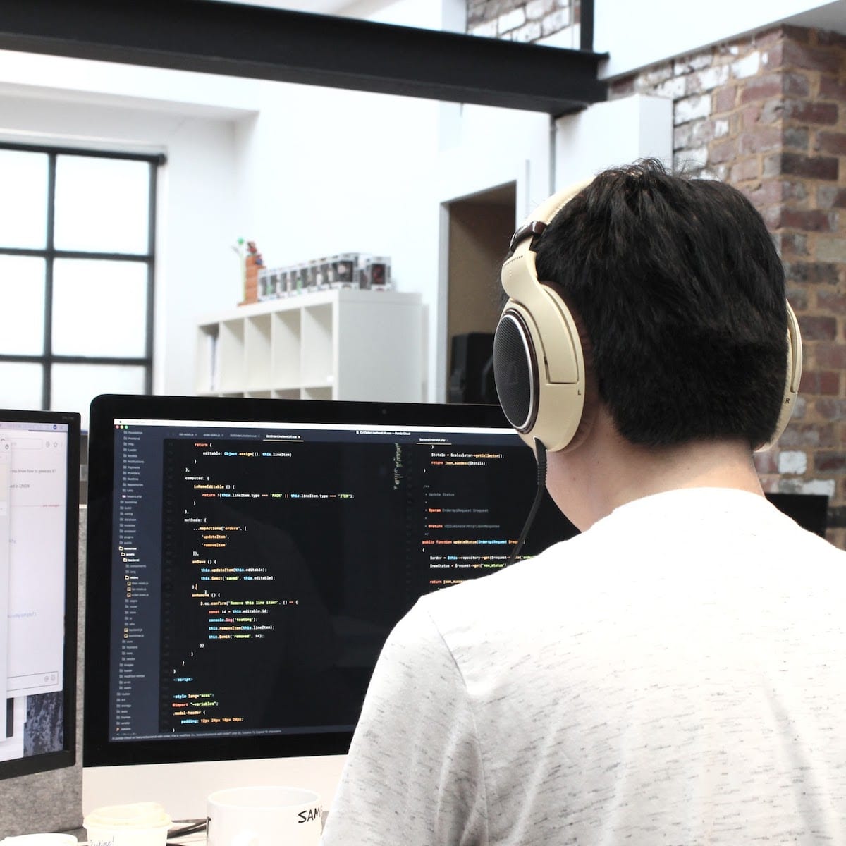 Man with headphones on looks at computor monitor showing code. 