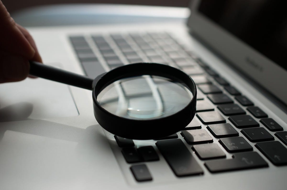 A hand holding a magnifying glass over a laptop keyboard.