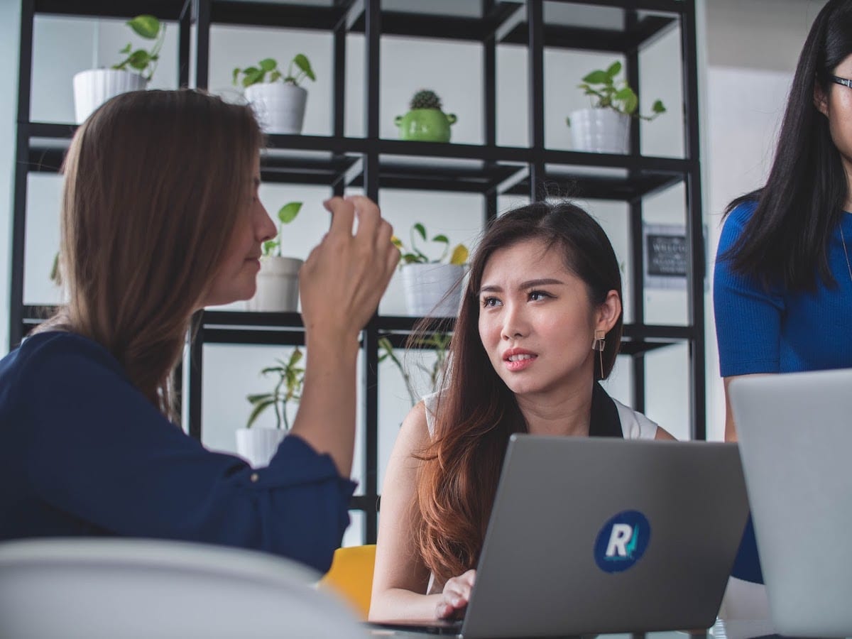 Image of women collaborating around a laptop.