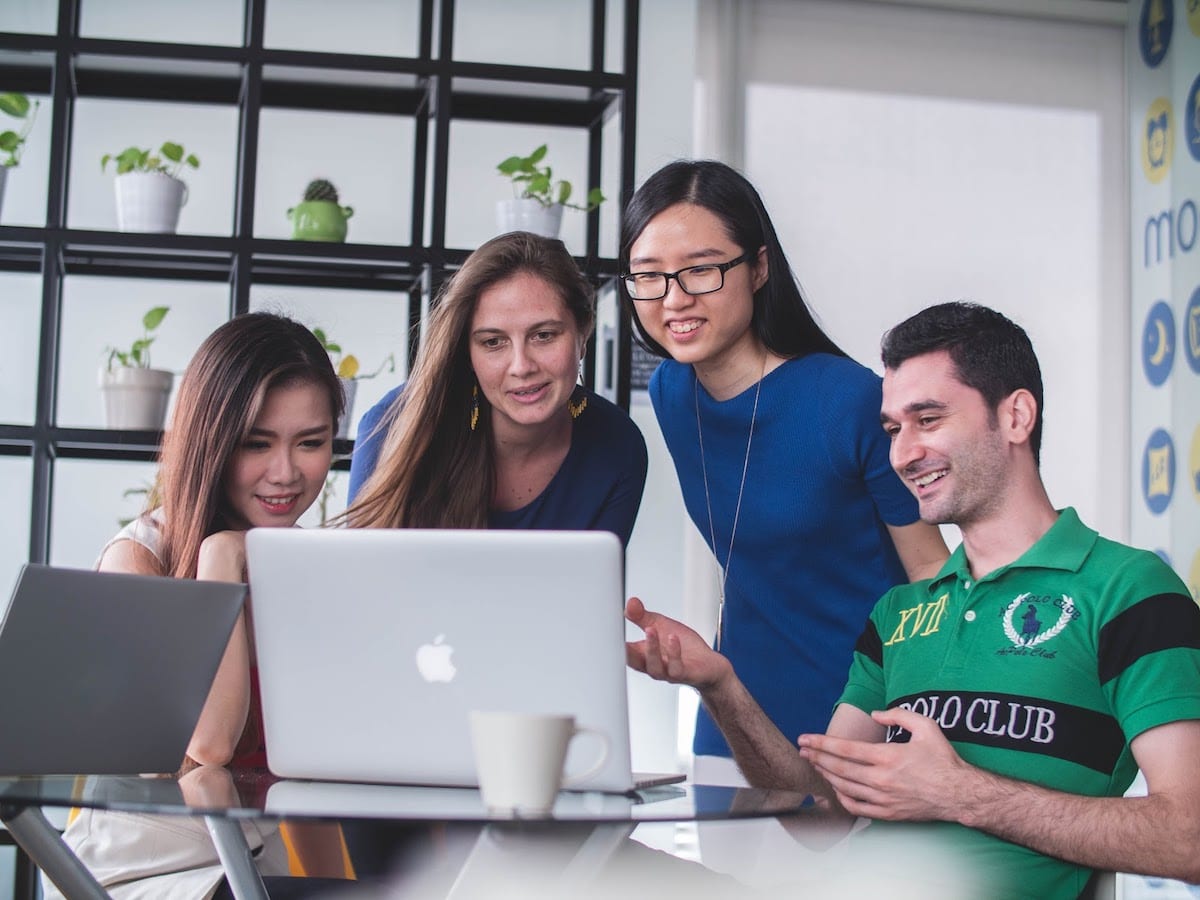 Four smiling students gathered around a laptop.