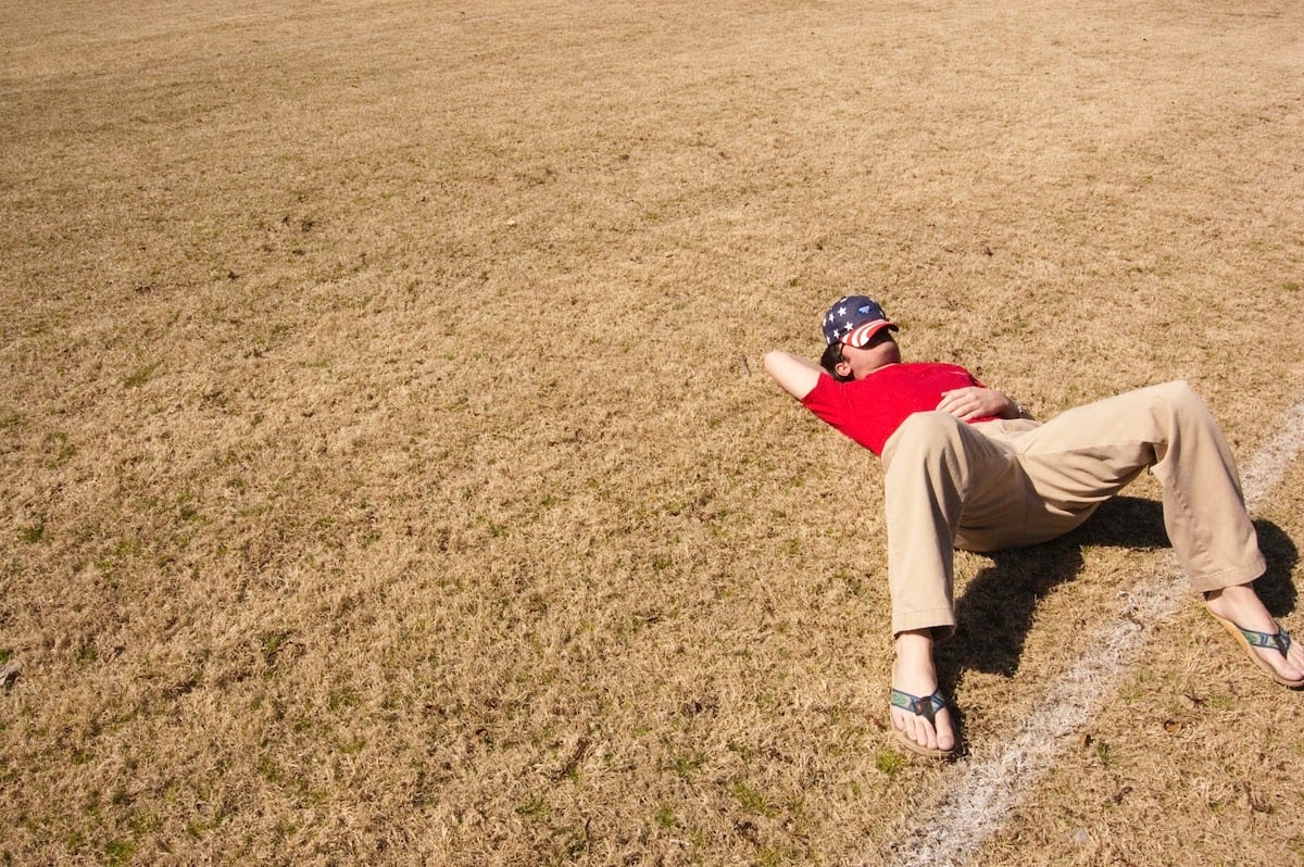 A person lying in a field with a hat over their face
