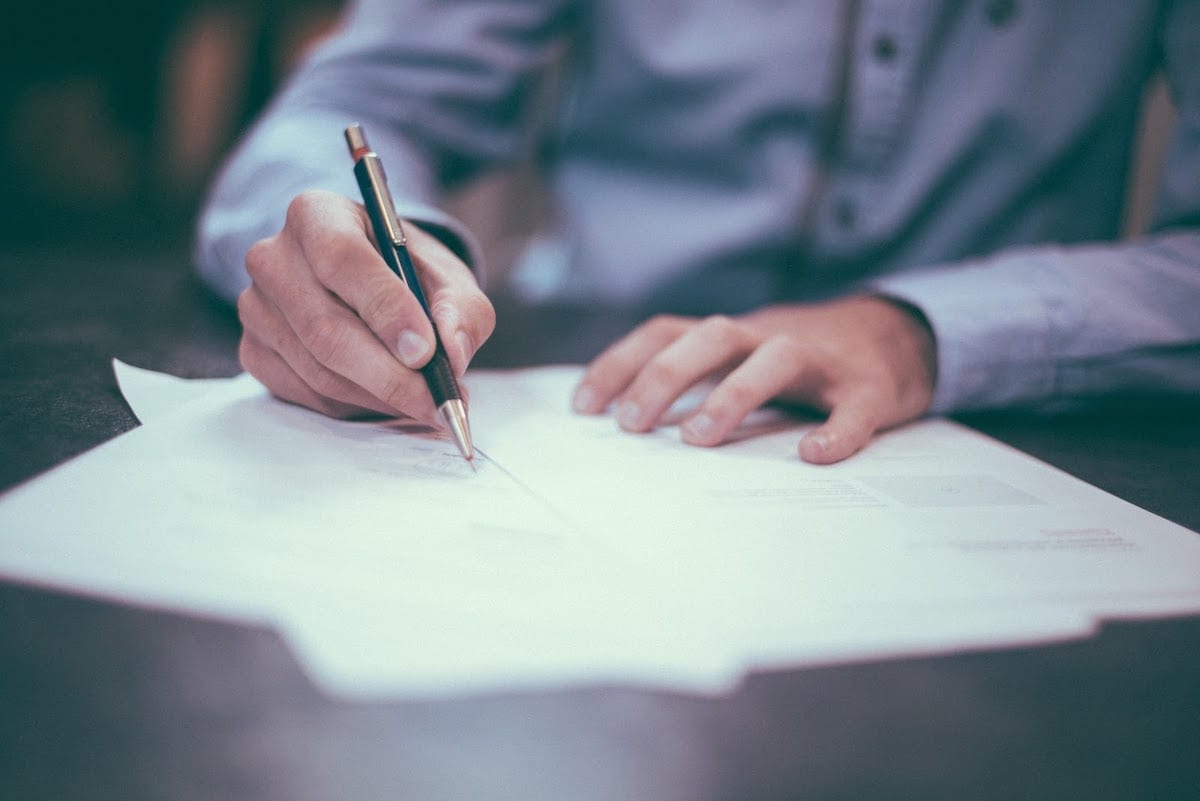 A UC Riverside bootcamp student in a blue shirt signing papers with a black and gold pen.