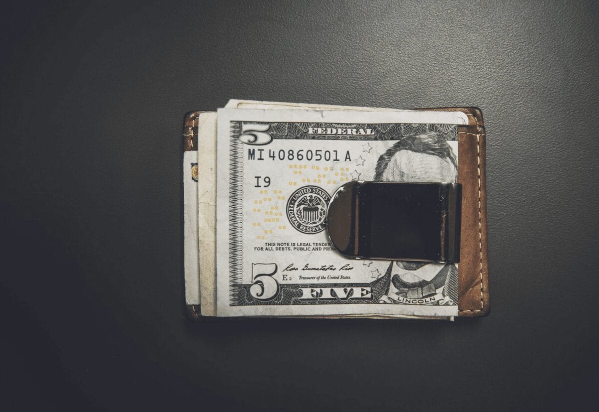 An image of a money clip on a wallet holding a five-dollar bill.