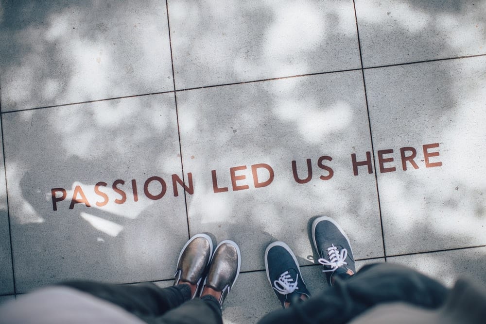  People standing over a message written on the sidewalk, reading “Passion Led Us Here.” 