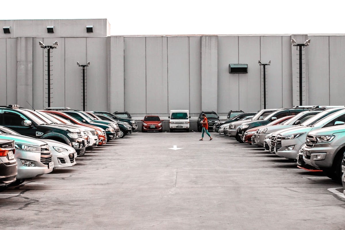 A parking lot with many cars and a pedestrian crossing.