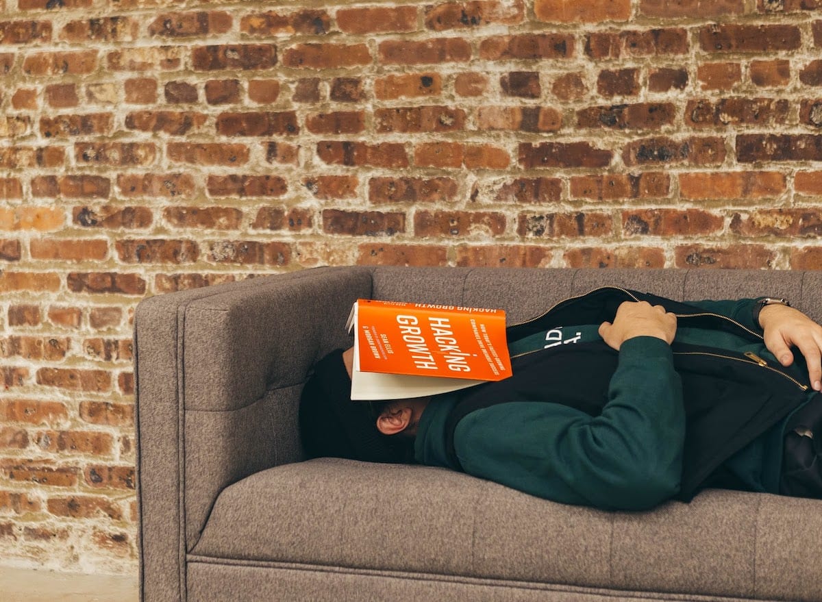 A tech professional asleep on the couch with a book about hacking covering their face