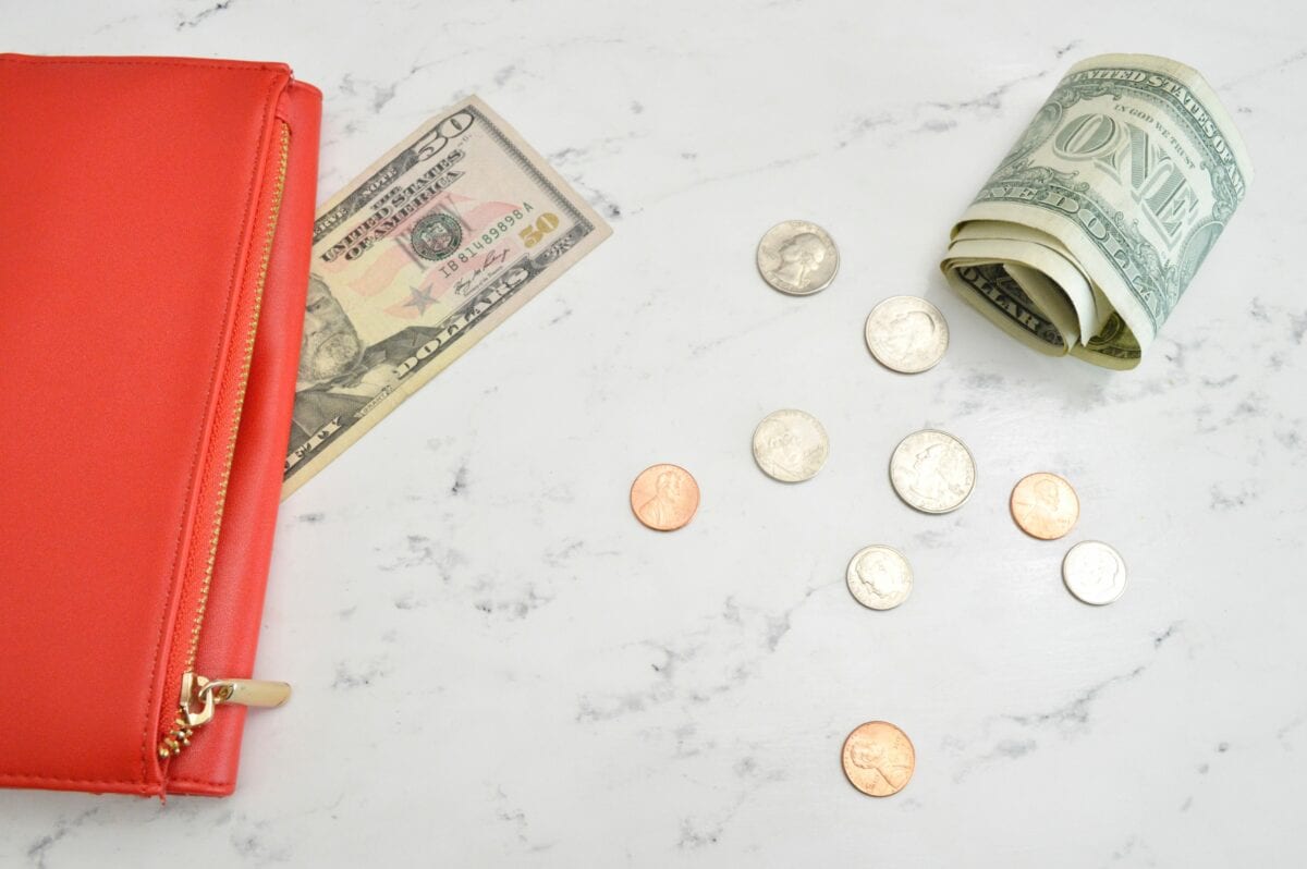 A red wallet on a white marble background with dollar bills and coins.