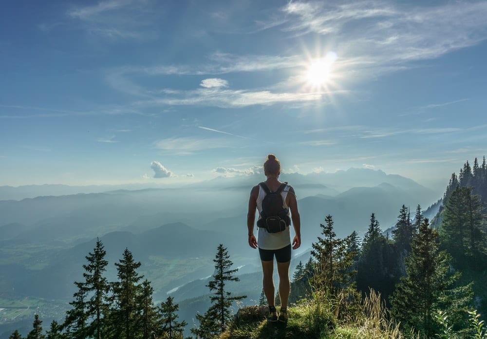 A climber stands at the top of a mountain overlooking a scenic view