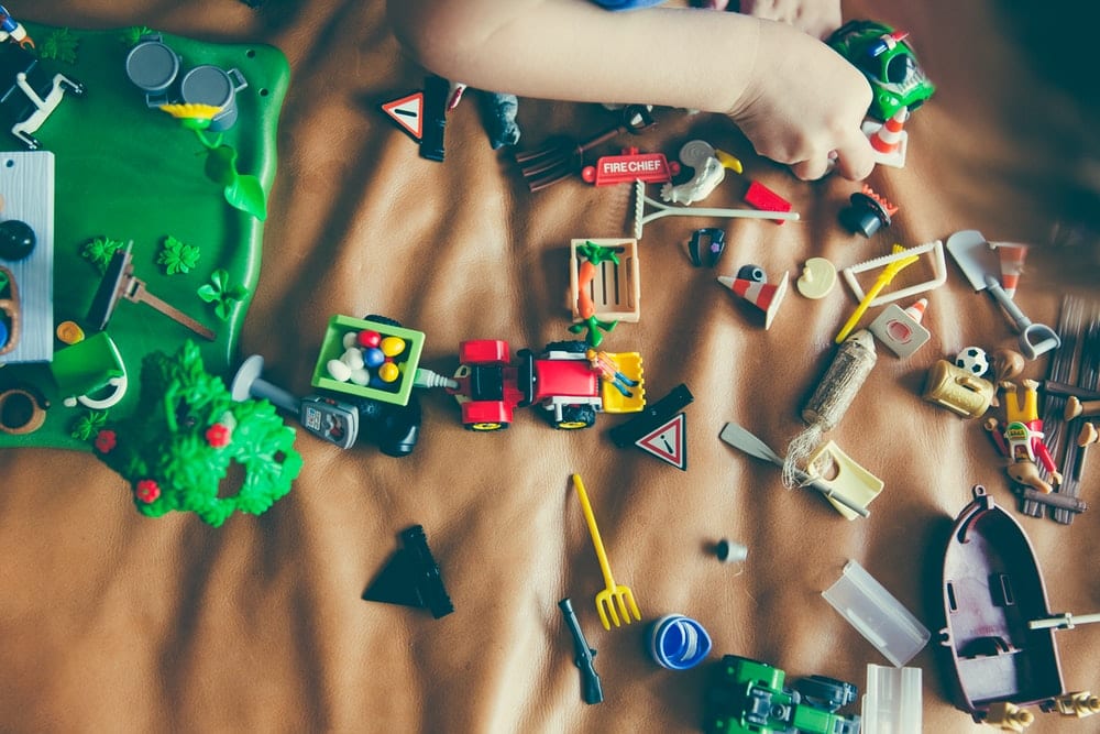 Two hands playing with a variety of small toys spread out over a brown blanket. 
