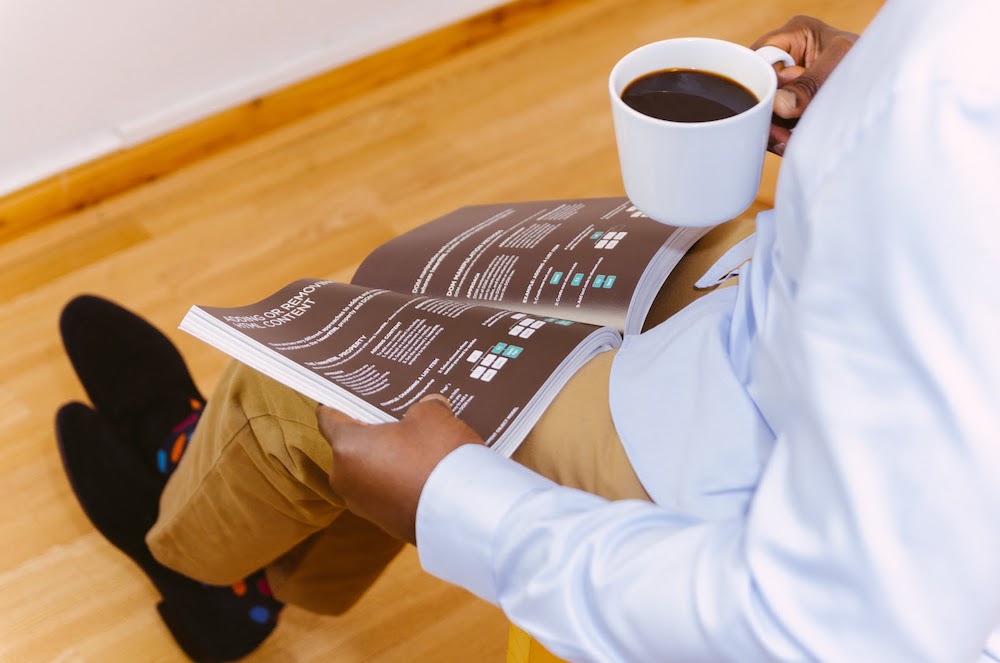 A coding apprenticeship participant holding a book open with one hand while holding a cup of coffee in another hand
