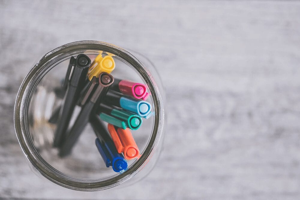 Various colored pens held in a glass jar. 