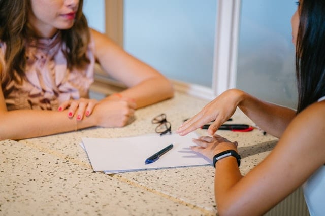 Two women conducting a technical interview at a table with a notepad, pens, and a pair of glasses in front of them 