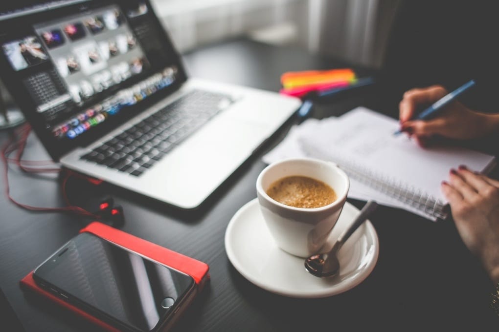 woman writing with coffee in front of a laptop