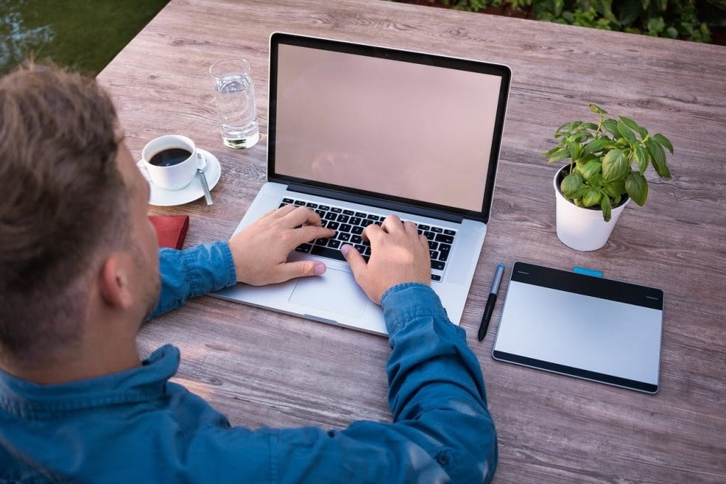 man typing at laptop with coffee and tablet