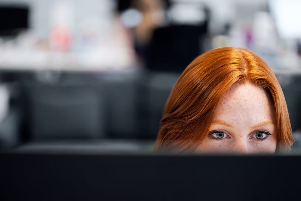 top of womans head behind computer monitor