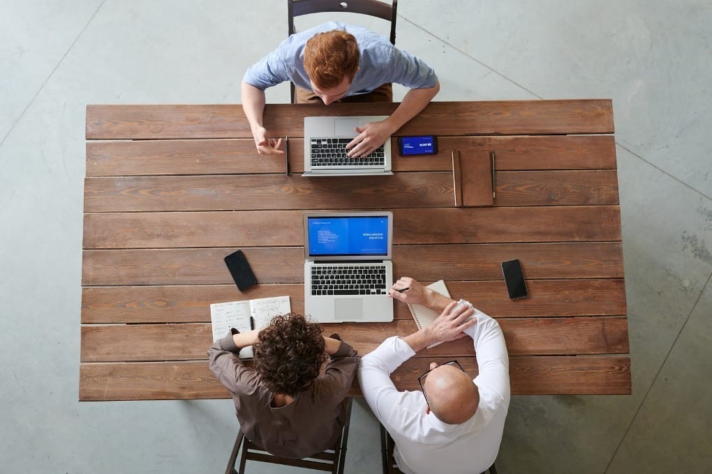 Three people in a discussion at a table with laptops