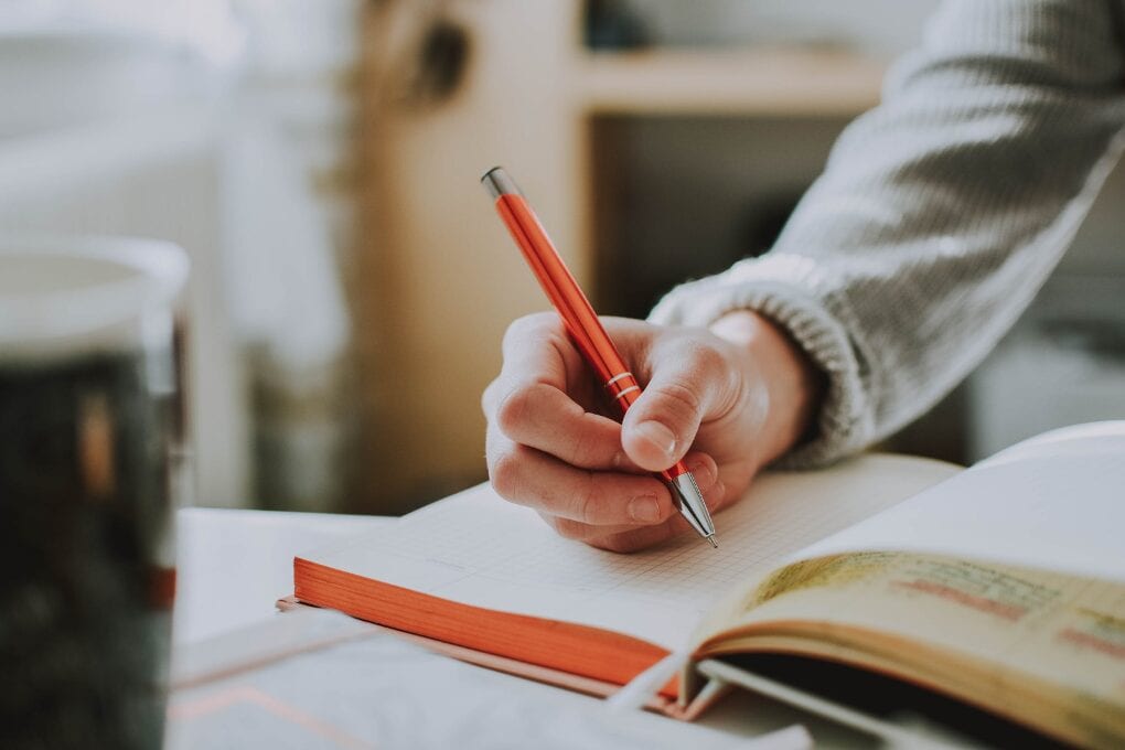 A prospective student taking notes on how to get into a coding bootcamp with a notebook and pen.
