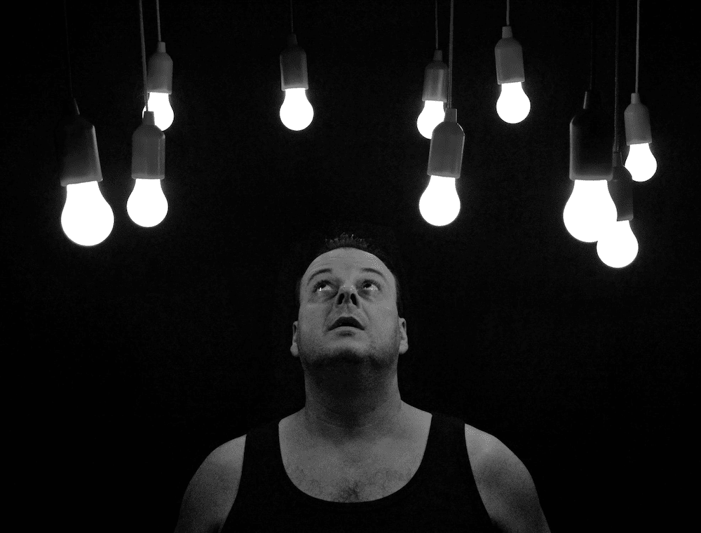 A person looking up at a number of lit bulbs in a darkened room. 