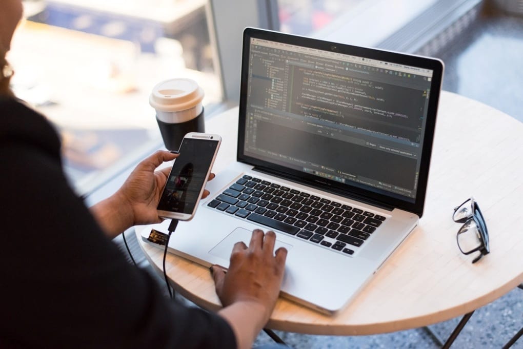 a woman holding phone while coding on laptop