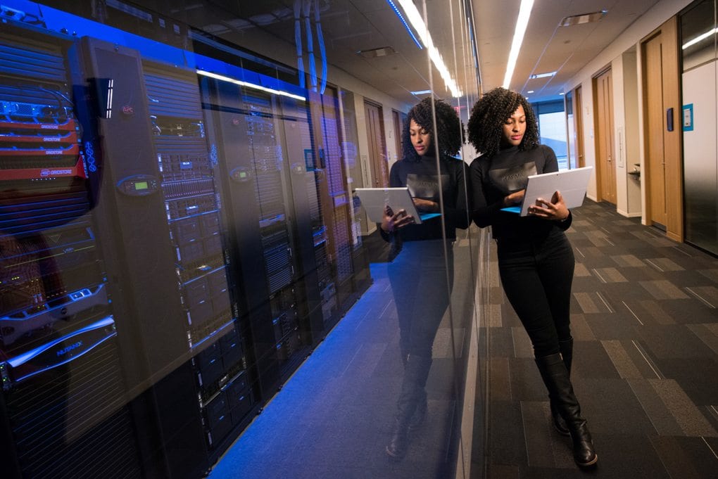 A woman stands in a hallway looking at data on her laptop computer.