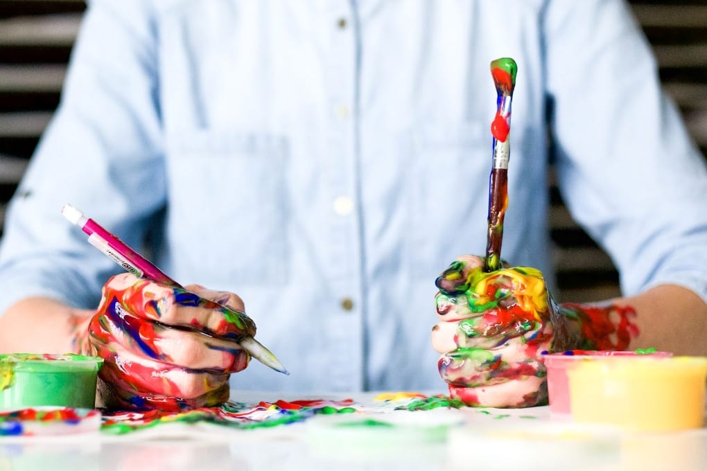 A person holding a paintbrush in one hand and a pencil in another