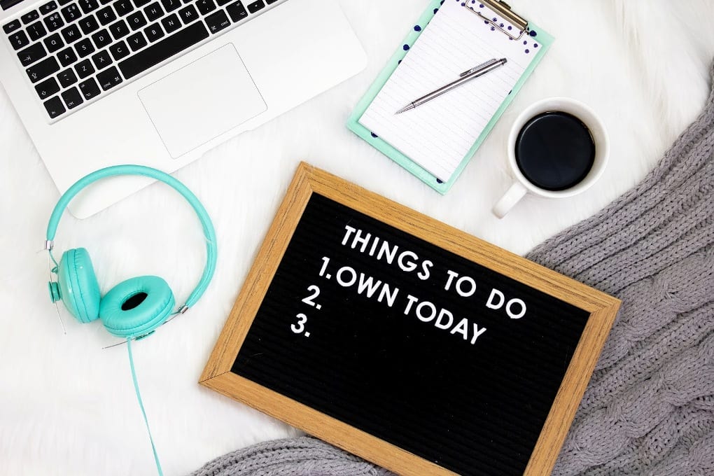 A board, notepad, laptop, coffee and headphones on a table.