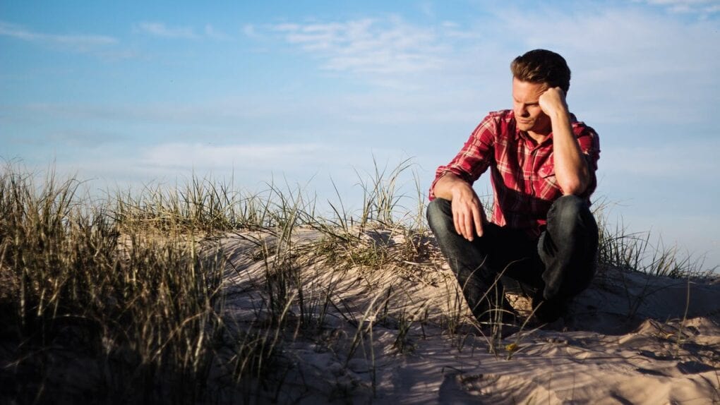 A man sits on a beach looking confused