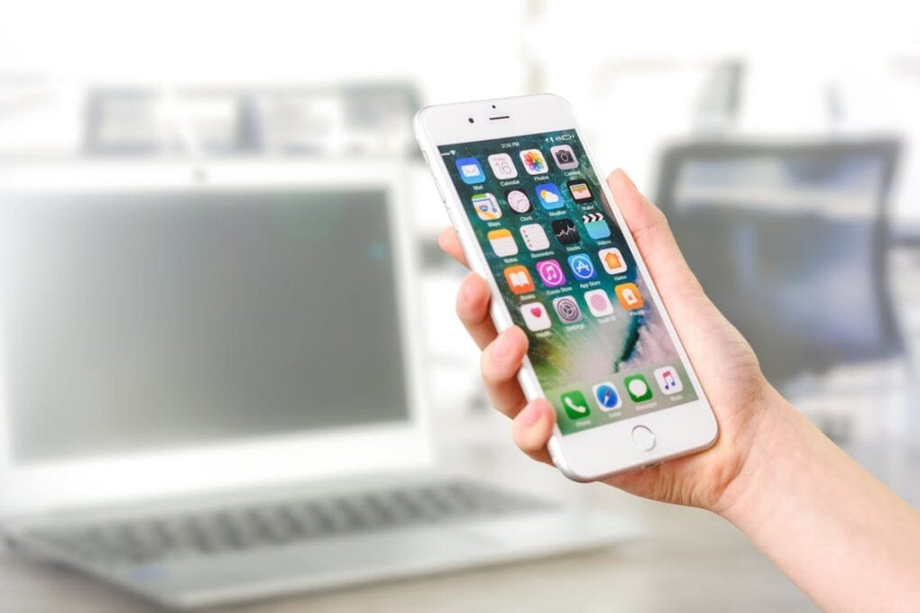 A person holds an iPhone in front of a laptop