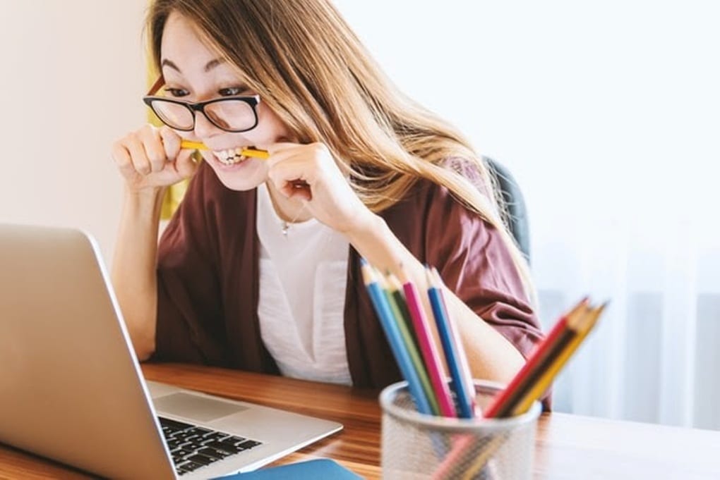 A person biting a pencil while staring at a laptop 