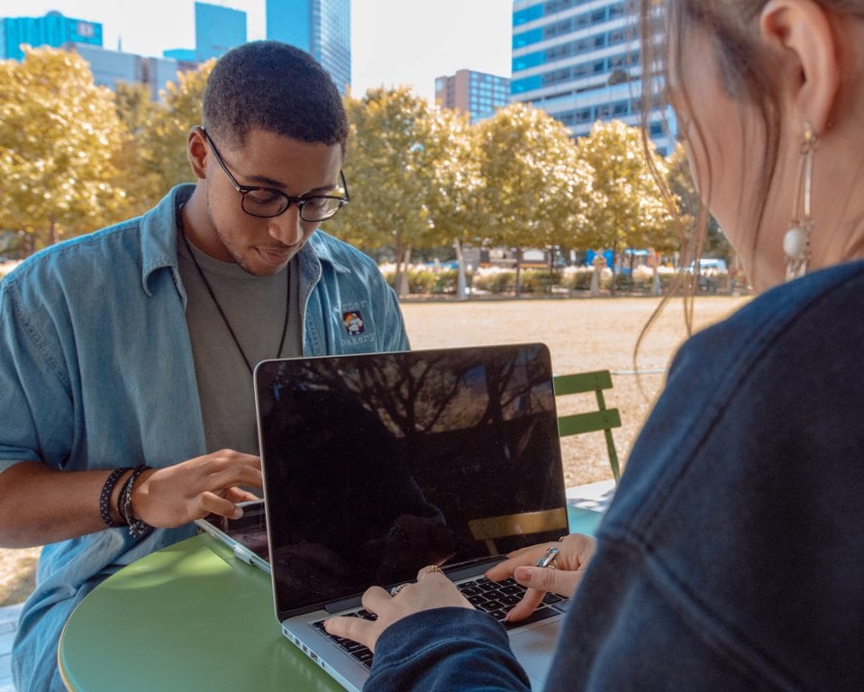 Man and woman both studying on separate laptops in outdoor park
