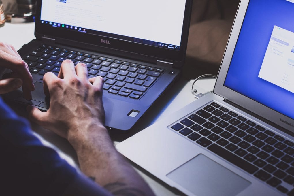 Person typing on one laptop with second laptop open next to him