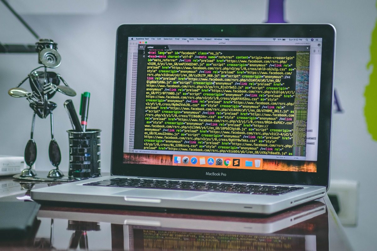 A Mac laptop with code next to a robot on a desk.