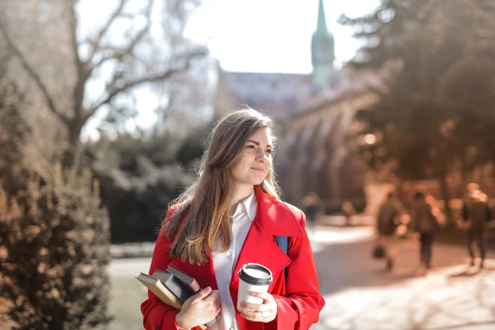 woman in red coat holding drink and books