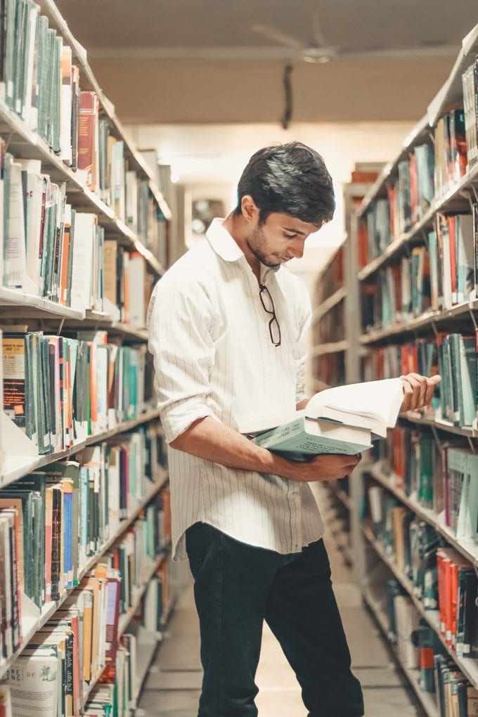 Student reads a book in a library aisle 