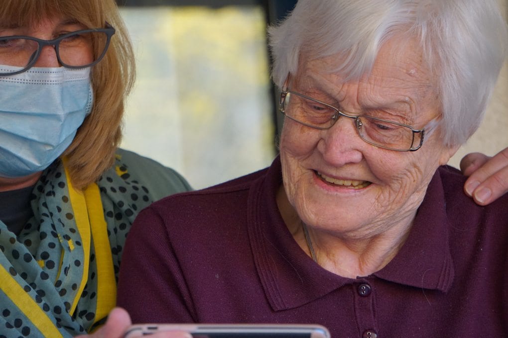 Two women, one younger, one elderly woman, look at an image on a phone
