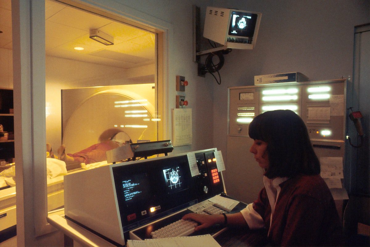 A person in a red shirt sitting in front of an MRI machine Health Informatics Master's Degrees: Best Programs, Jobs, and Salaries