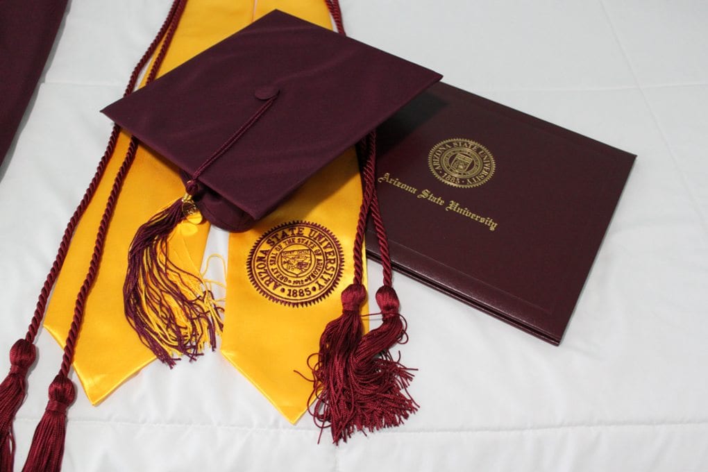 a diploma, graduation cap, and regalia lie displayed on a white surface
