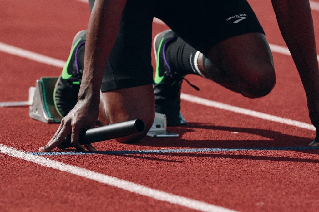 a close up of a runner's feet on the running track and his arms on the floor as he is about to race.