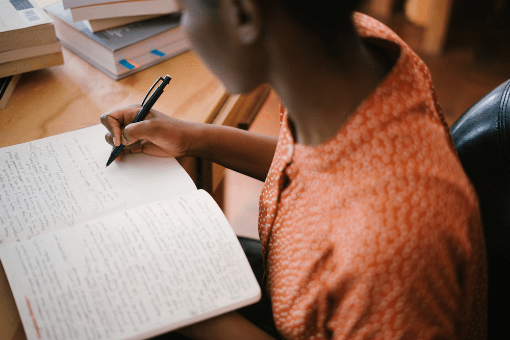 A woman writes in a notebook to calculate her GPA from her unweighted classes and weighted classes