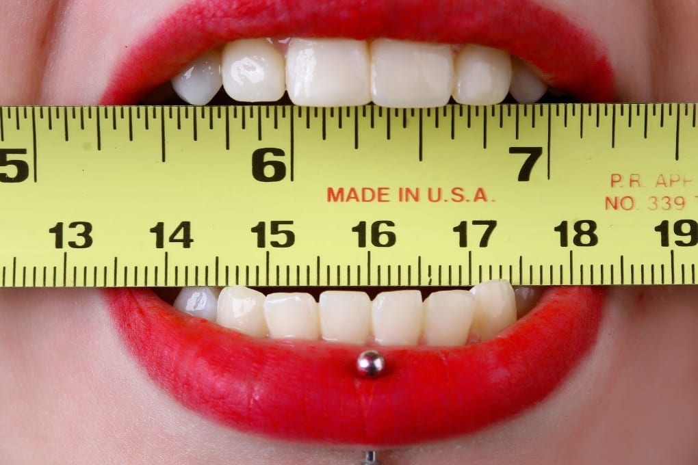 A woman’s lips with a ruler between her teeth 