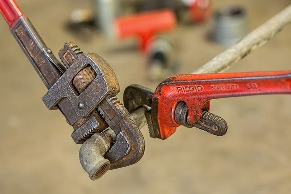 Plumbing pipe being repaired with a wrench.