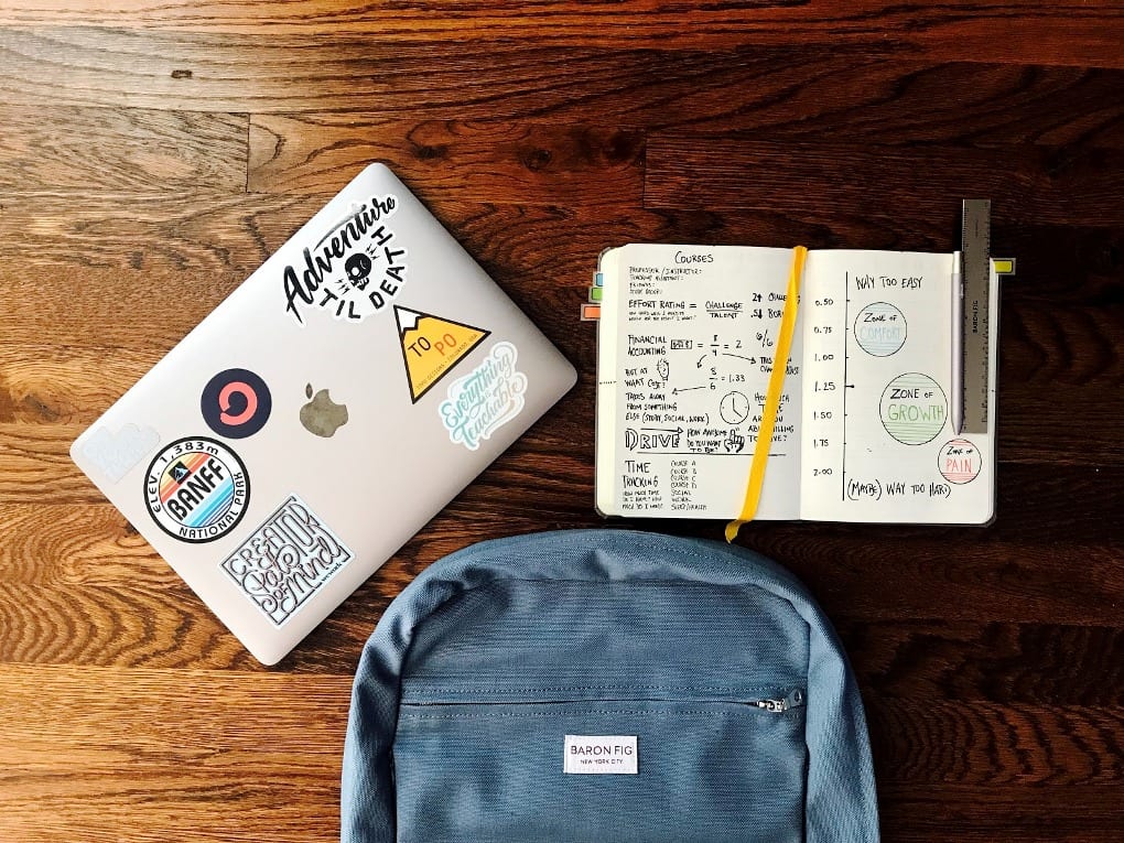 a laptop with stickers on it next to a blue rucksack and a notebook