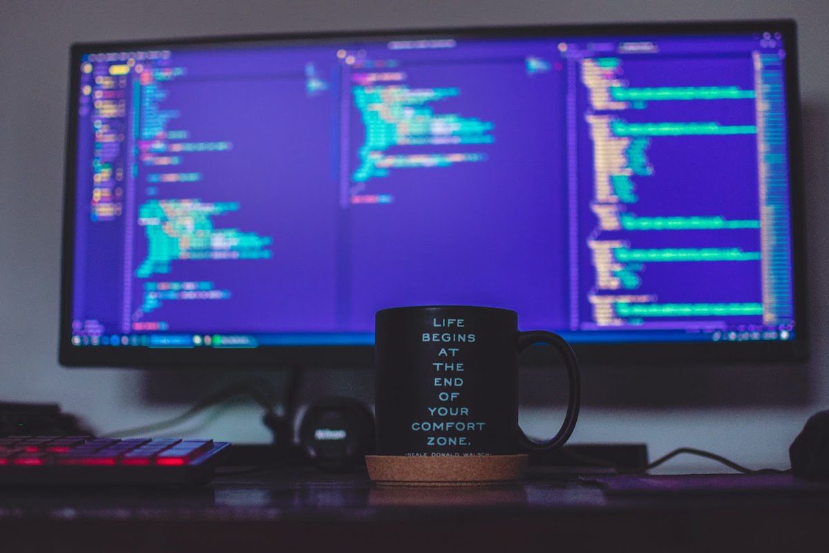 Black coffee mug on a desk in front of a screen displaying code