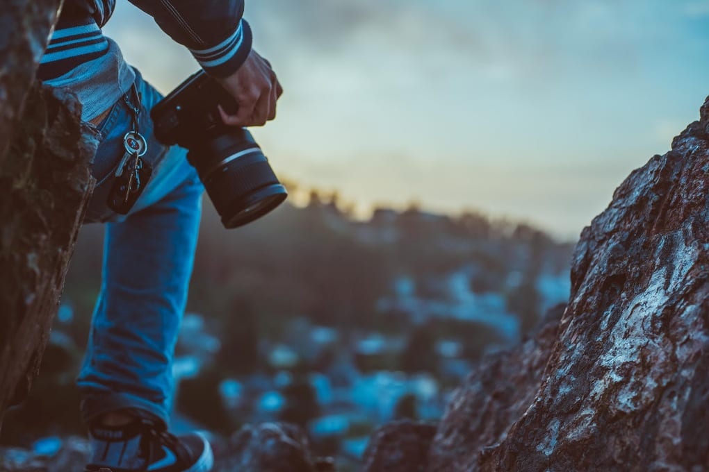 a man’s leg stands on a rocky cliff with a camera on his hip
