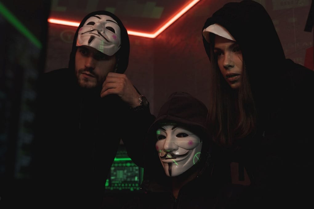 Three hackers wearing masks in front of a computer.