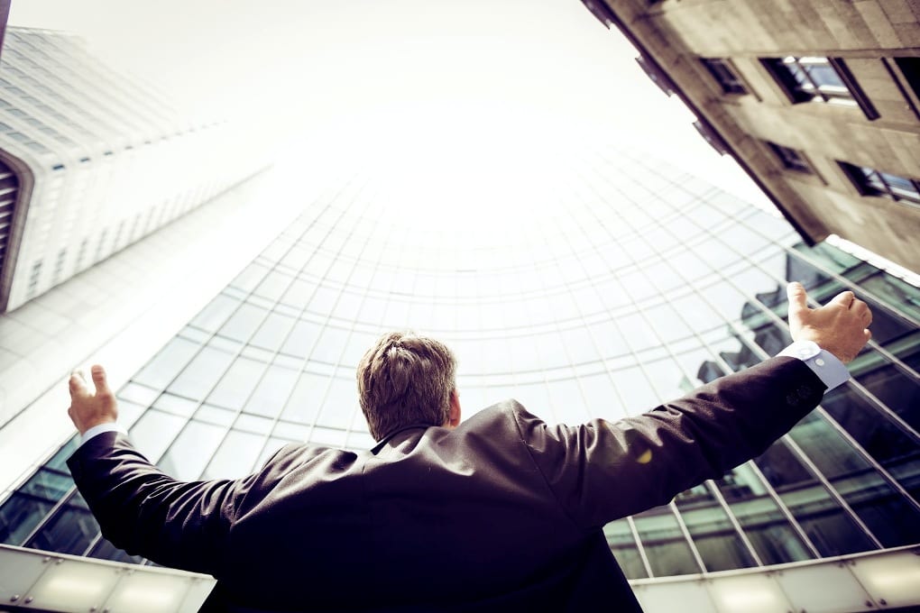 Man in suit raising arms above head and looking up at tall buildings
